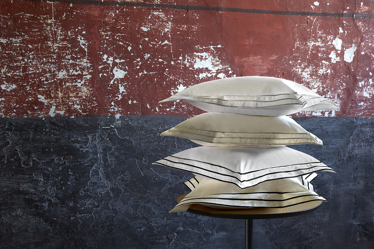 Stack of four Alba pillow shams in varying ivory and champagne tones with contrast borders.