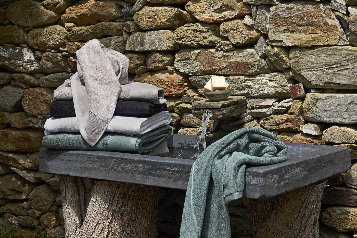 Stack of folded towels on a wooden bench against a stone wall.