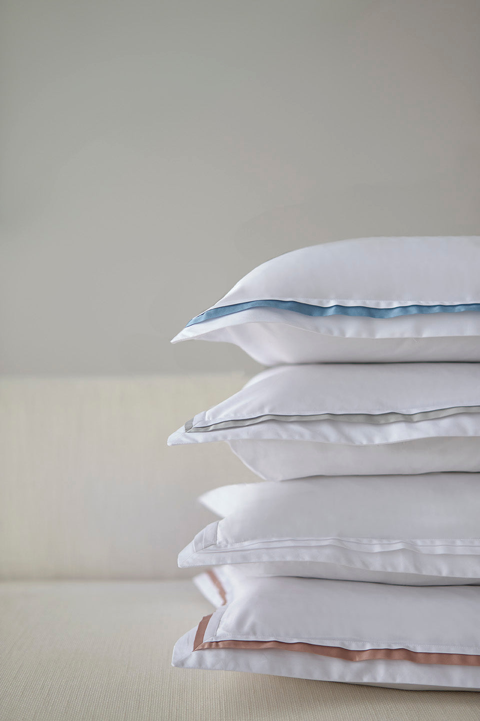 Close-up stack of white cotton pillow shams with contrast border trim in blue, grey, and blush.