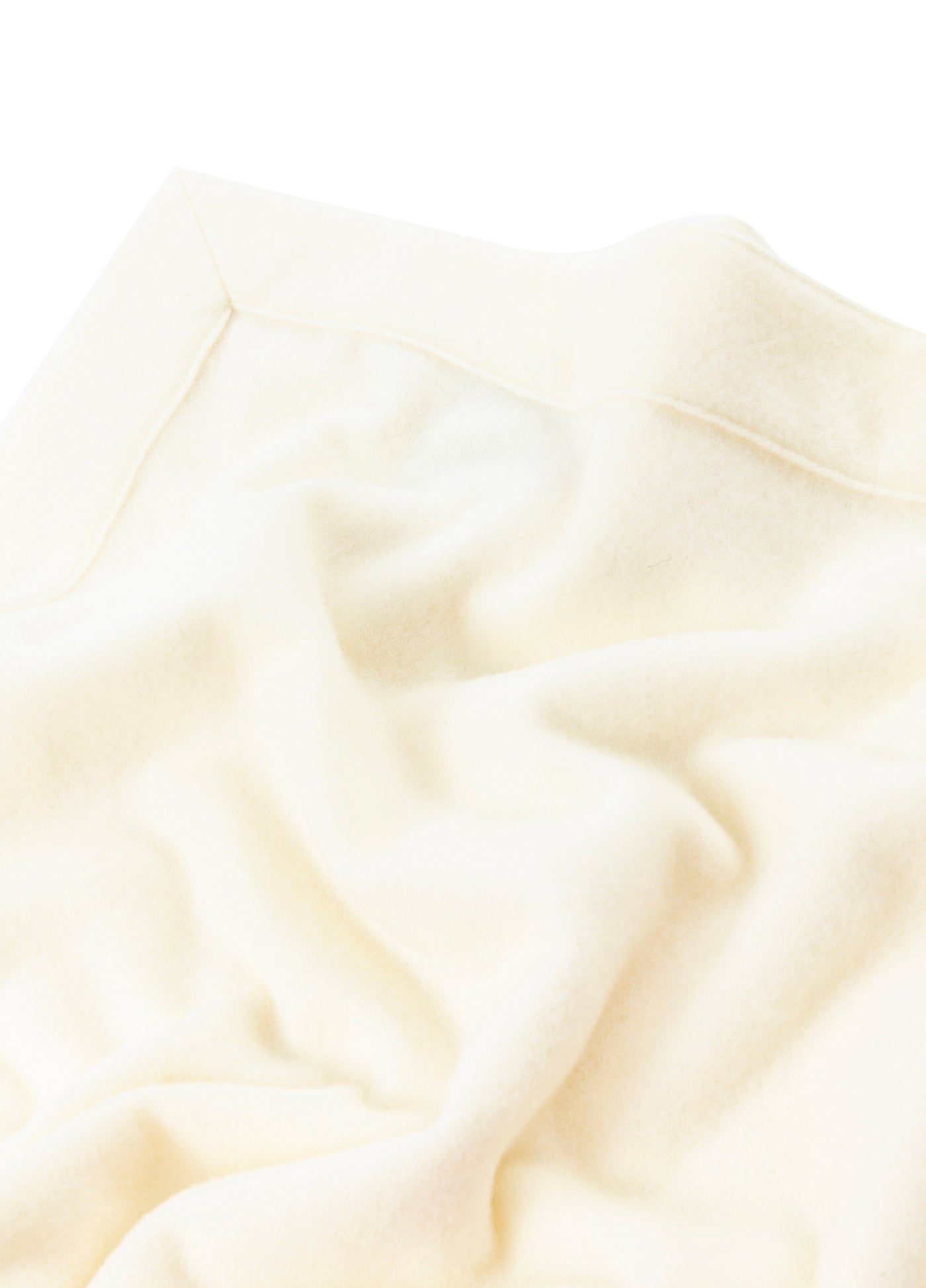 Close-up of ivory wool blanket corner showing hem detail and soft draped folds.