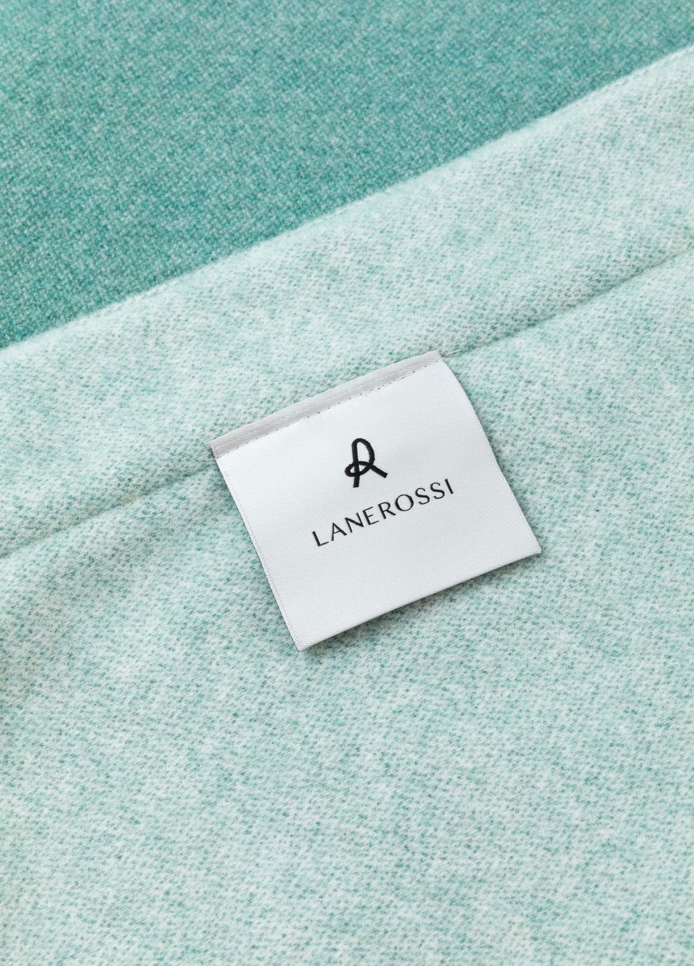 Close-up of Lanerossi woven label on aqua melange wool blanket corner.