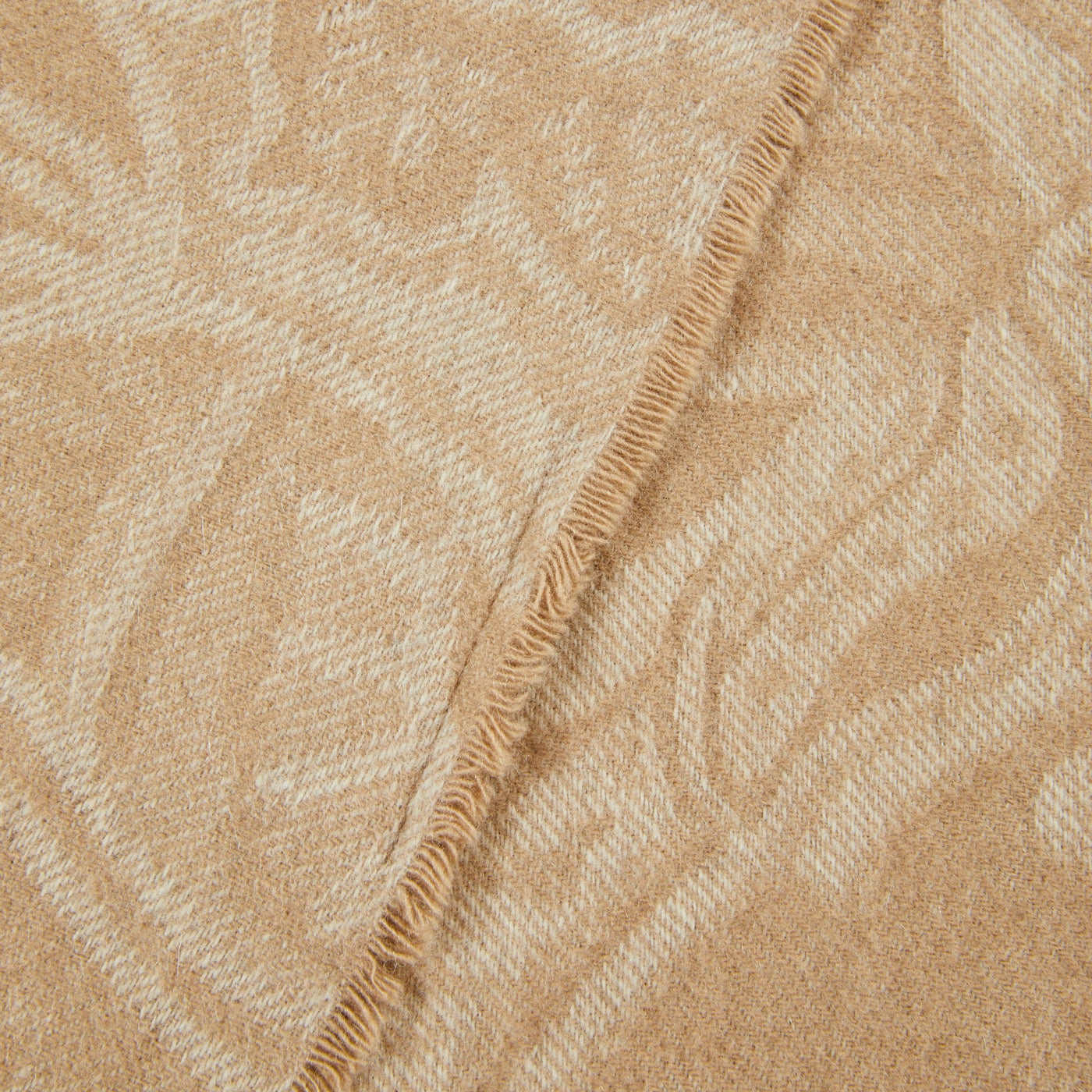 Close-up of camel and ivory jacquard throw corner with fringe trim and botanical pattern.