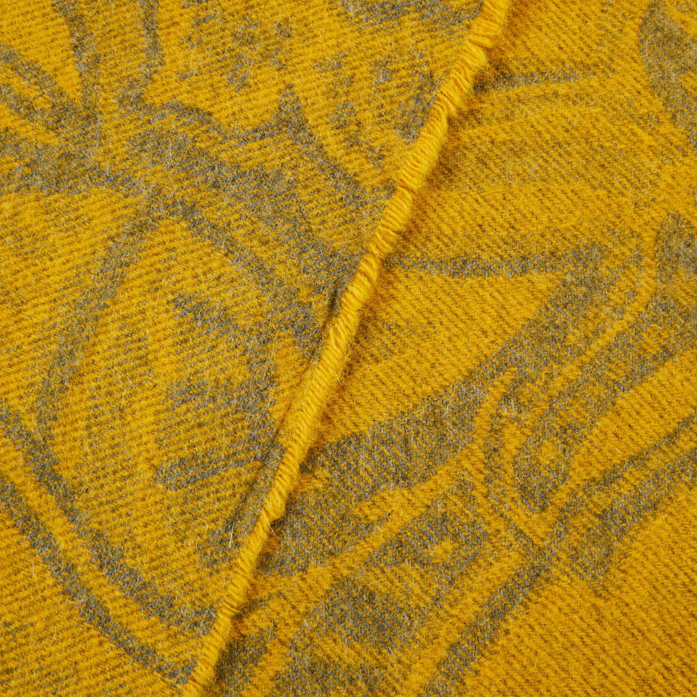 Close-up of saffron jacquard throw with botanical motif and contrast blanket-stitched edge.