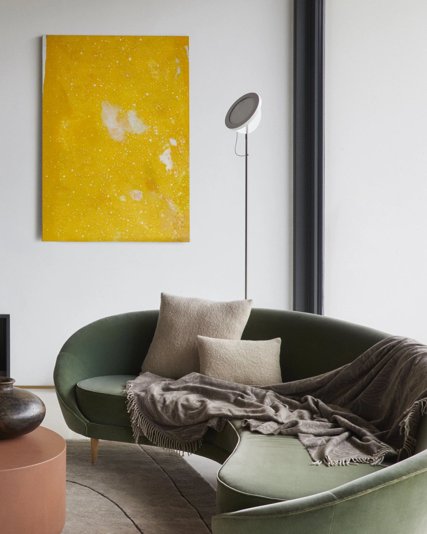 Taupe fringed throw draped over a green curved sofa in a modern living room.