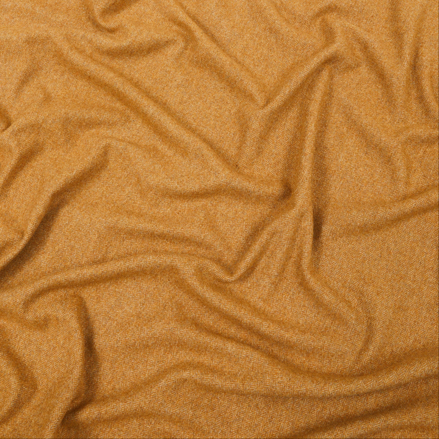 Close-up of draped camel wool throw fabric showing soft folds and fine heathered texture.