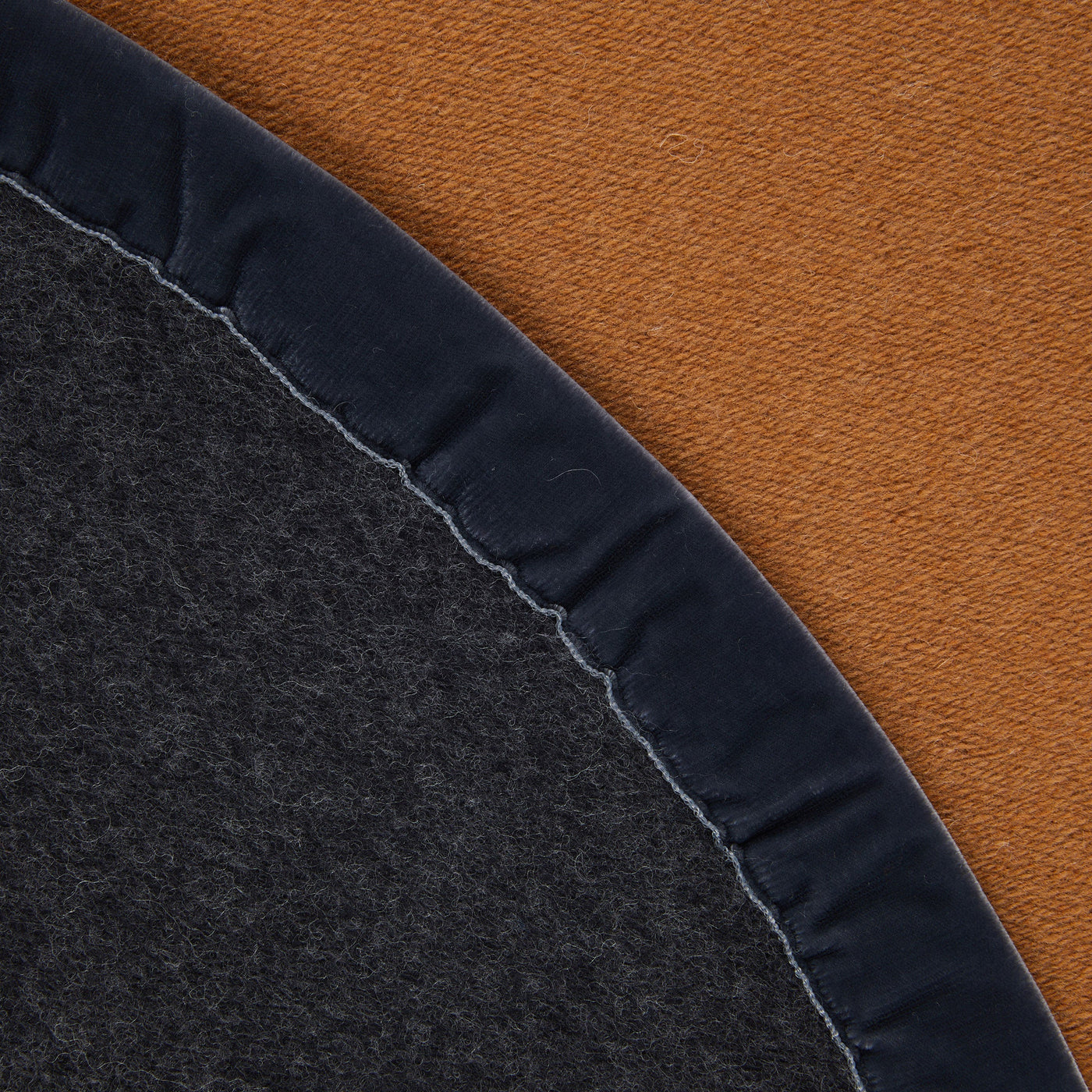 Close-up of charcoal blanket edge with navy velvet binding against a cognac background.