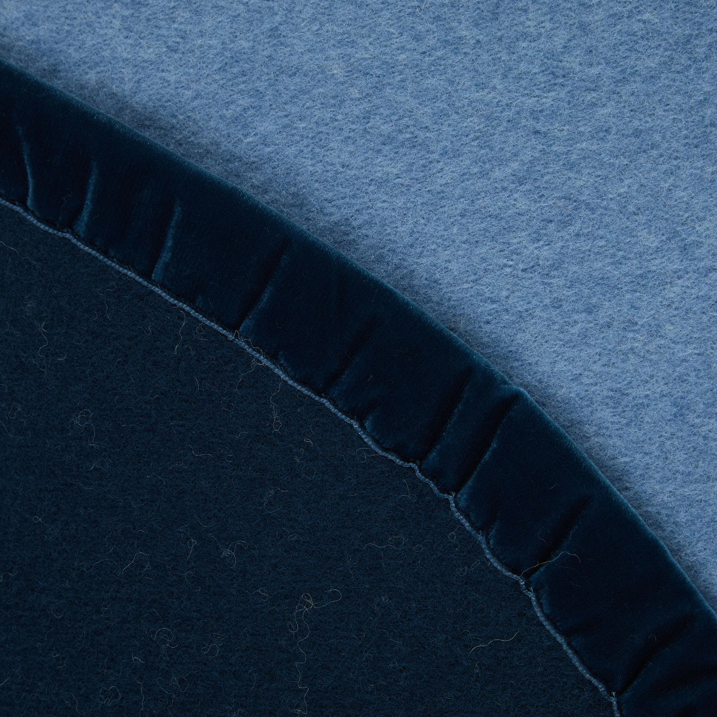 Close-up of navy and steel blue wool blanket edge with gathered velvet trim detail.
