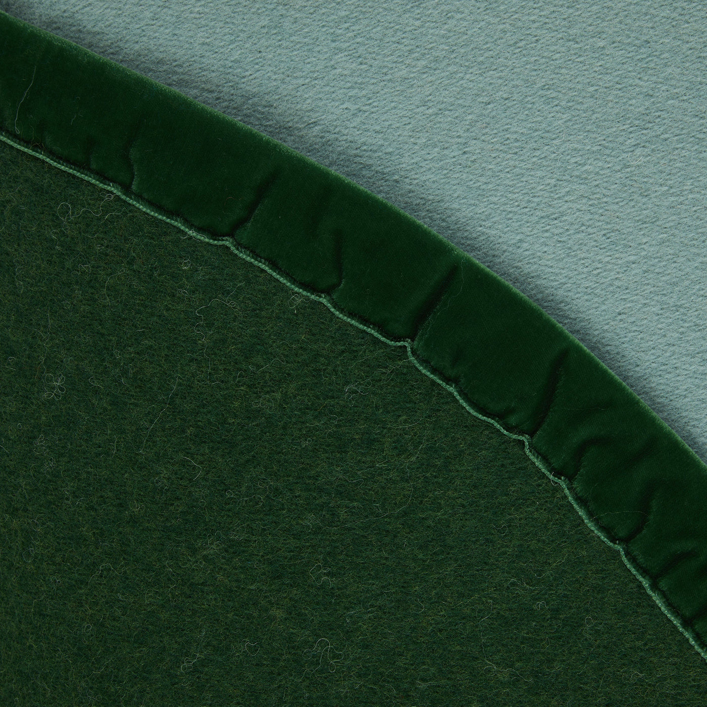 Close-up of forest green wool blanket edge with velvet ruffle trim against sage reverse.