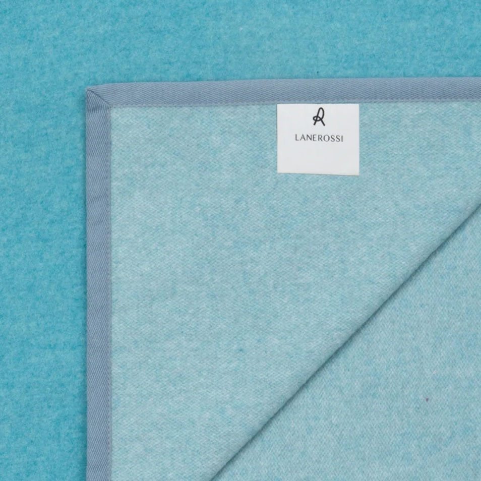 Corner detail of a Lanerossi Cortina blanket in aqua with a slate blue woven border trim.