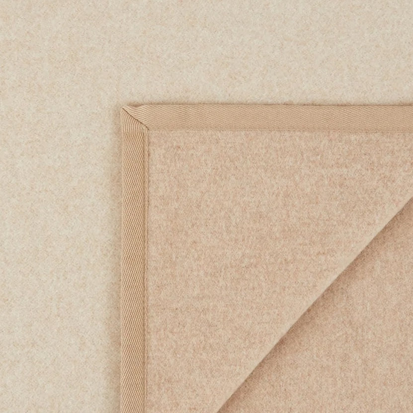 Corner detail of a sandstone wool blanket with woven satin binding trim.