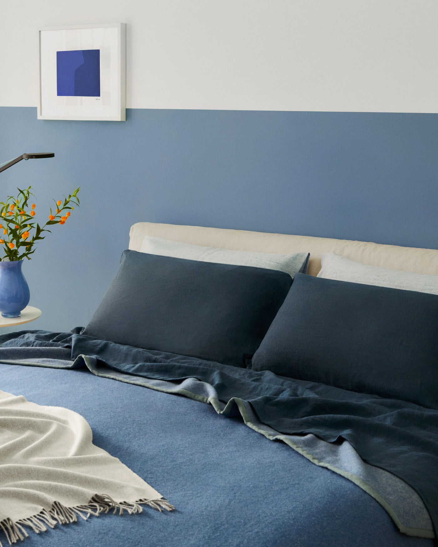 Lanerossi Cortina blanket in slate blue, draped over a styled bed with navy linen bedding.