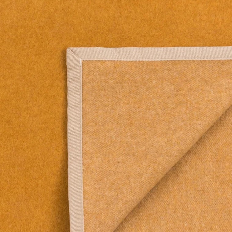 Corner detail of Lanerossi Cortina blanket in amber, showing ivory herringbone binding trim.