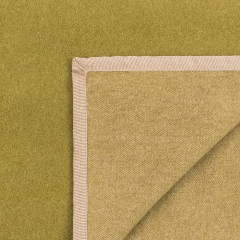 Close-up of folded chartreuse wool blanket corner showing ivory blanket-stitch trim detail.