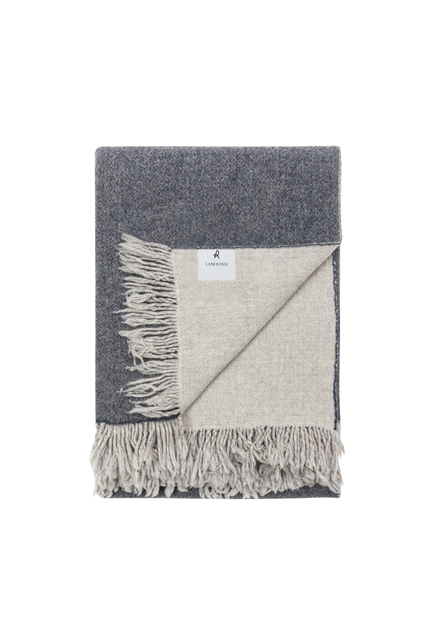 Folded Dioniso throw corner detail showing slate and ivory reversible weave with fringe trim.