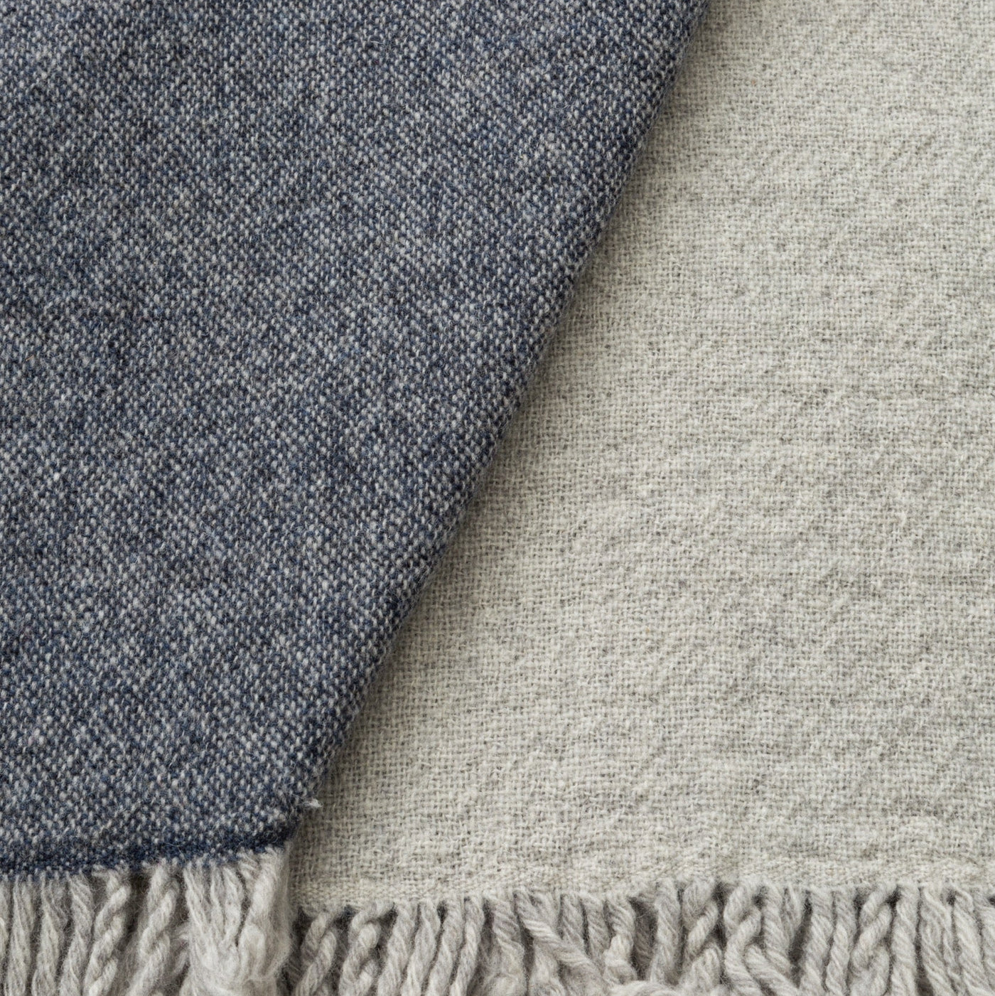 Close-up of two Dioniso throws in charcoal and oatmeal, showing woven texture and fringe detail.