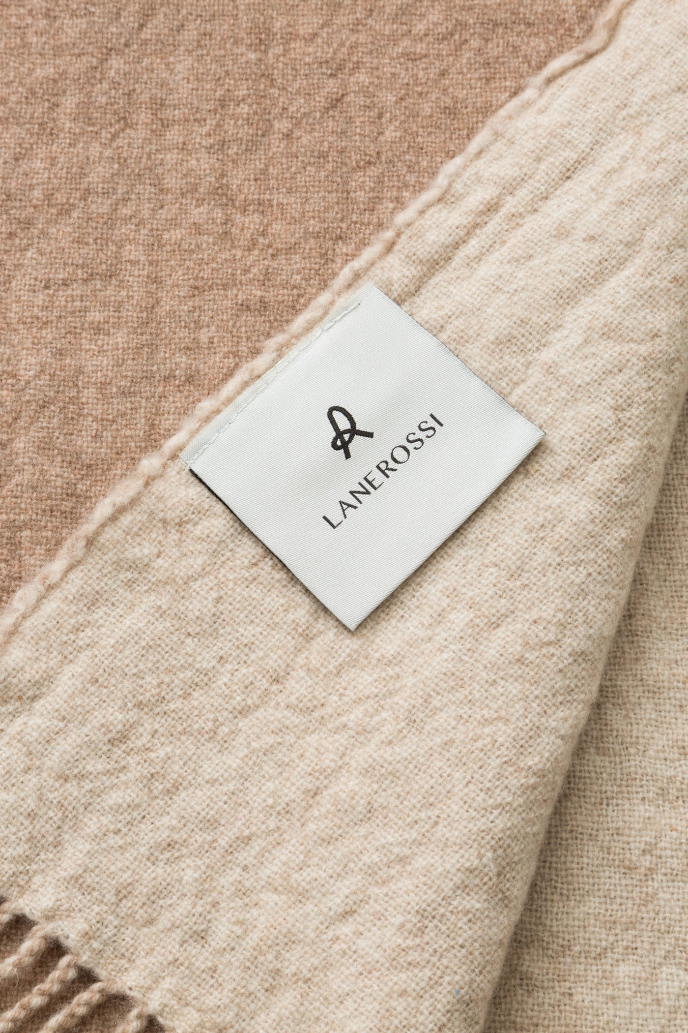 Close-up of Lane Rossi Dioniso throw label, camel and ivory wool fabric with fringe edge.
