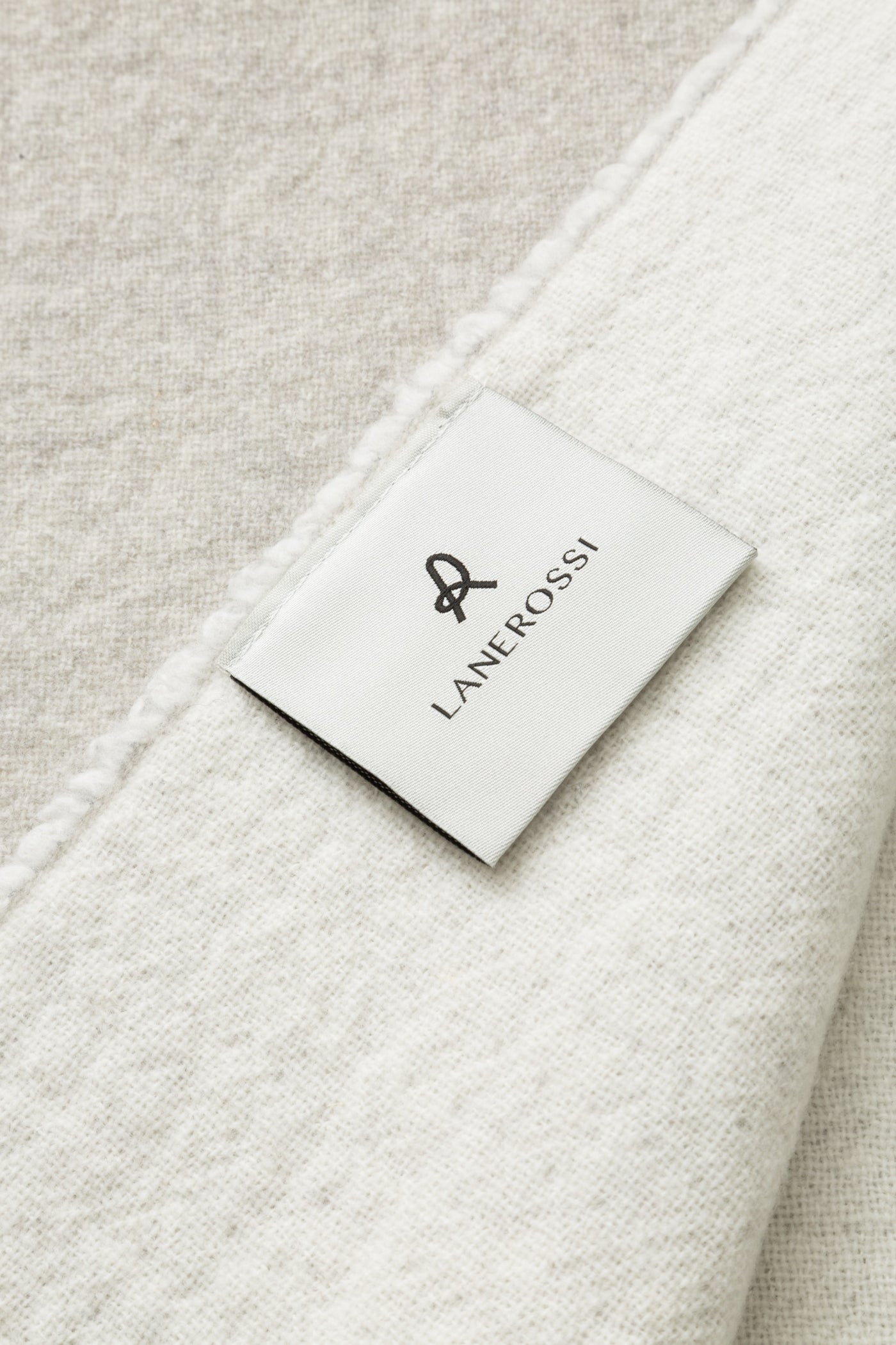 Close-up of Lanerossi Dioniso throw label on ivory textured fabric with contrast seam detail.