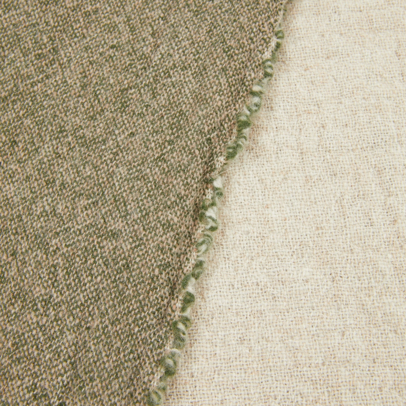 Close-up of Dioniso throw edge showing sage blanket-stitch trim between khaki and natural faces.