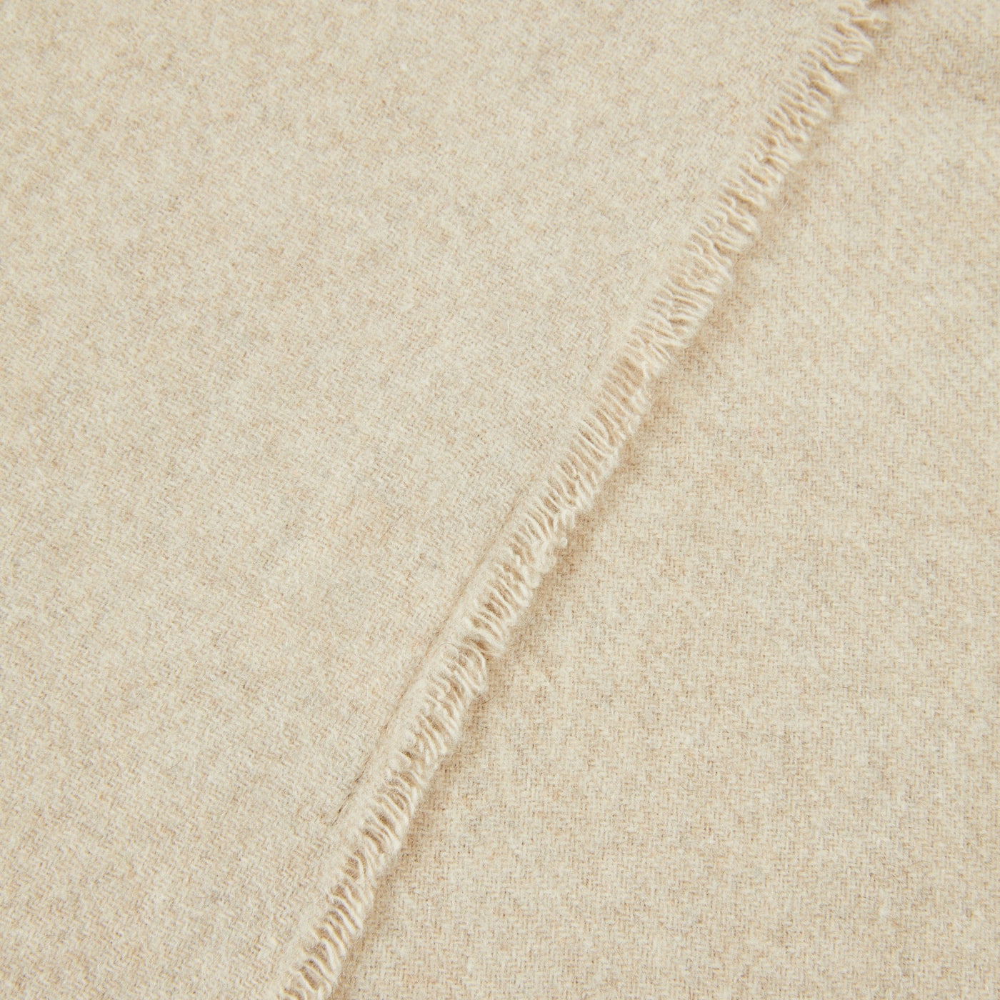 Close-up of ivory wool throw showing fringe edge detail and woven texture.