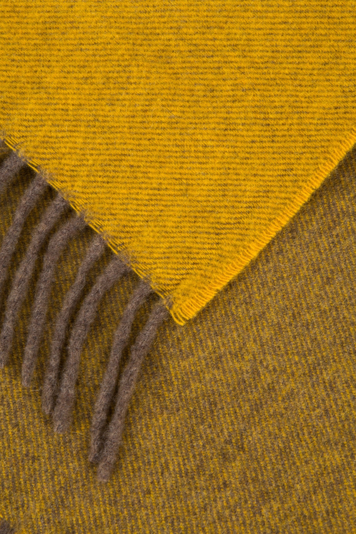 Close-up of folded corner revealing mustard and taupe reversible weave with taupe fringe trim.