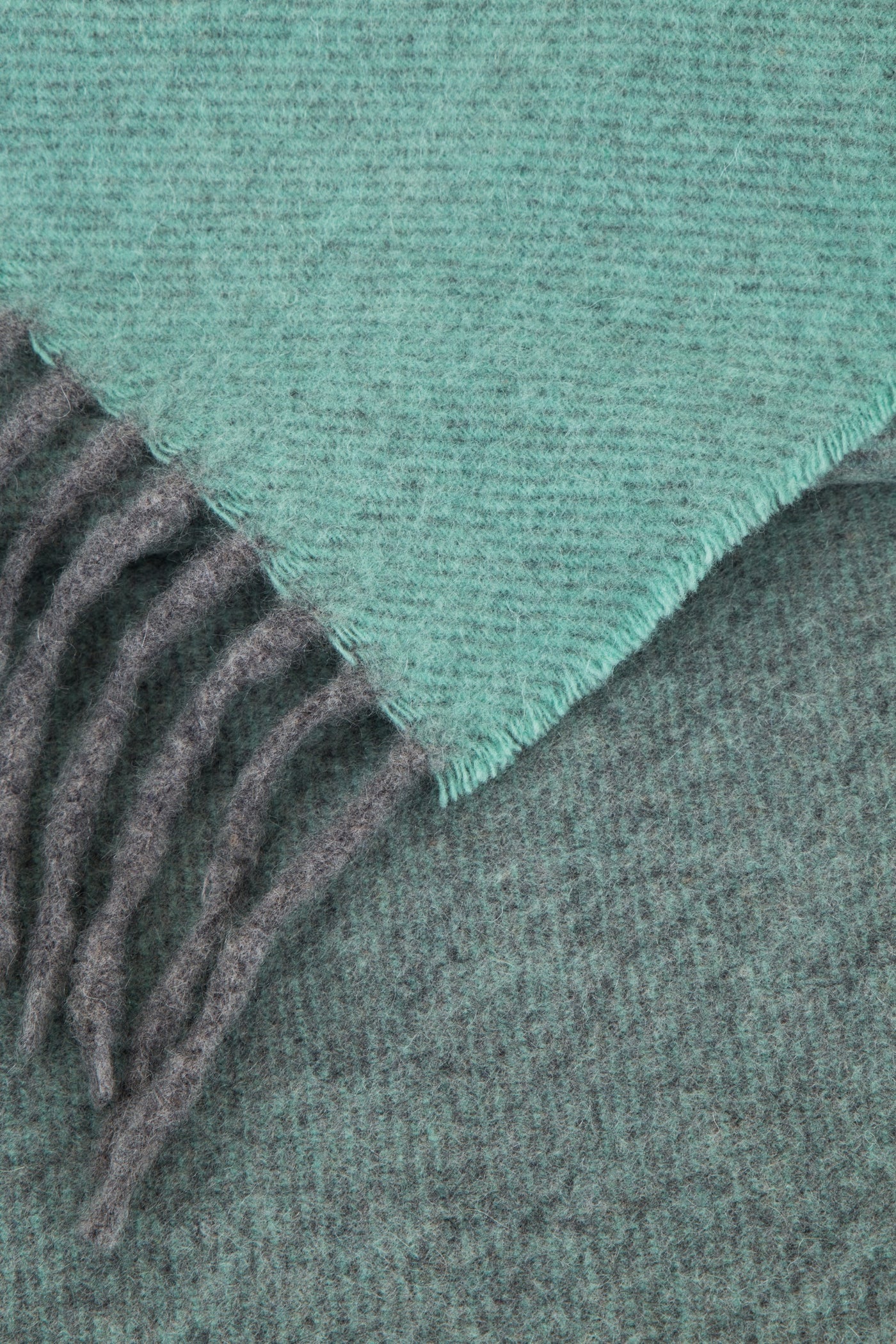 Close-up of aqua and charcoal reversible wool throw corner with knotted fringe detail.