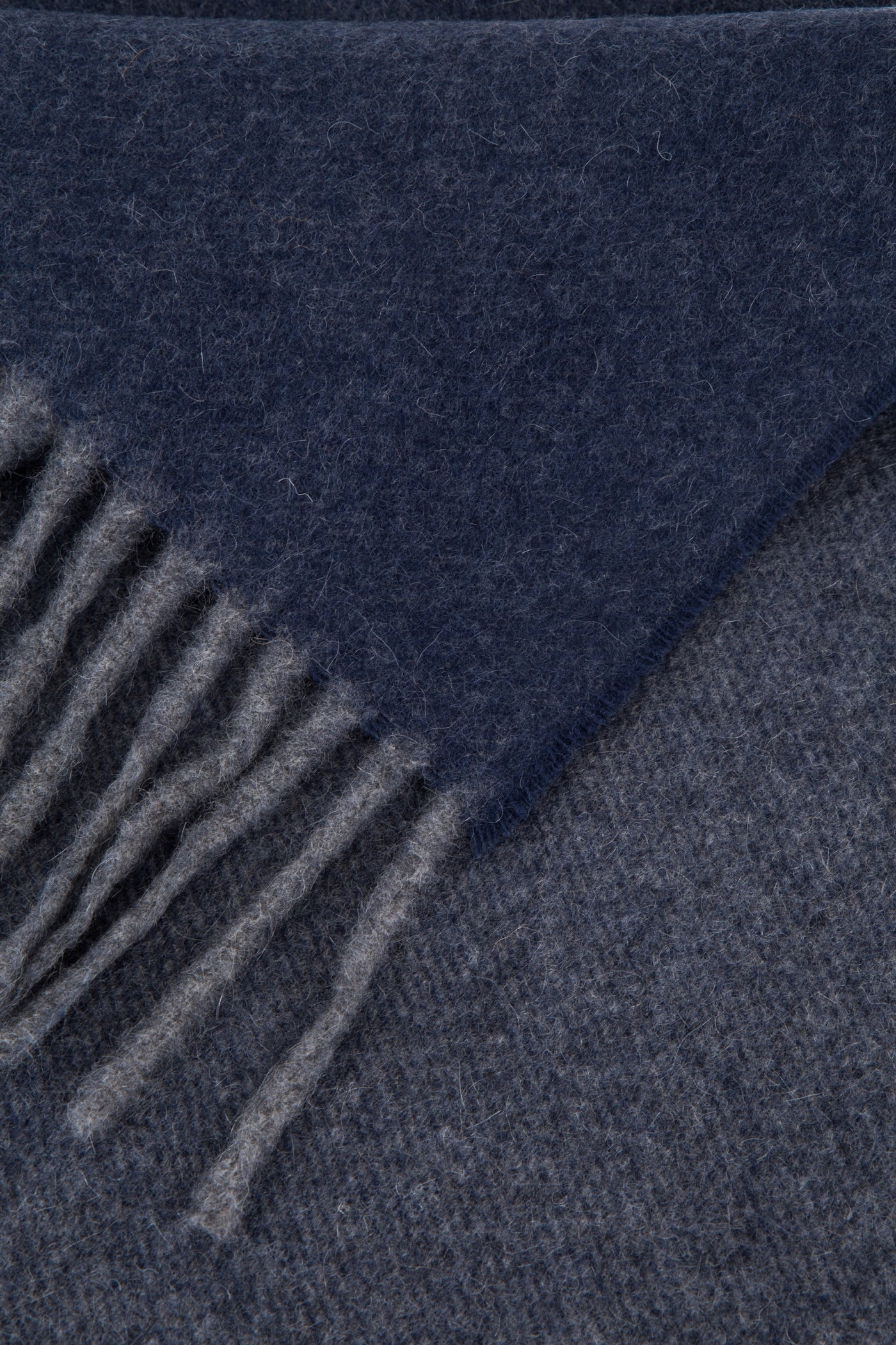 Close-up of navy and grey reversible wool throw corner with fringe detail.