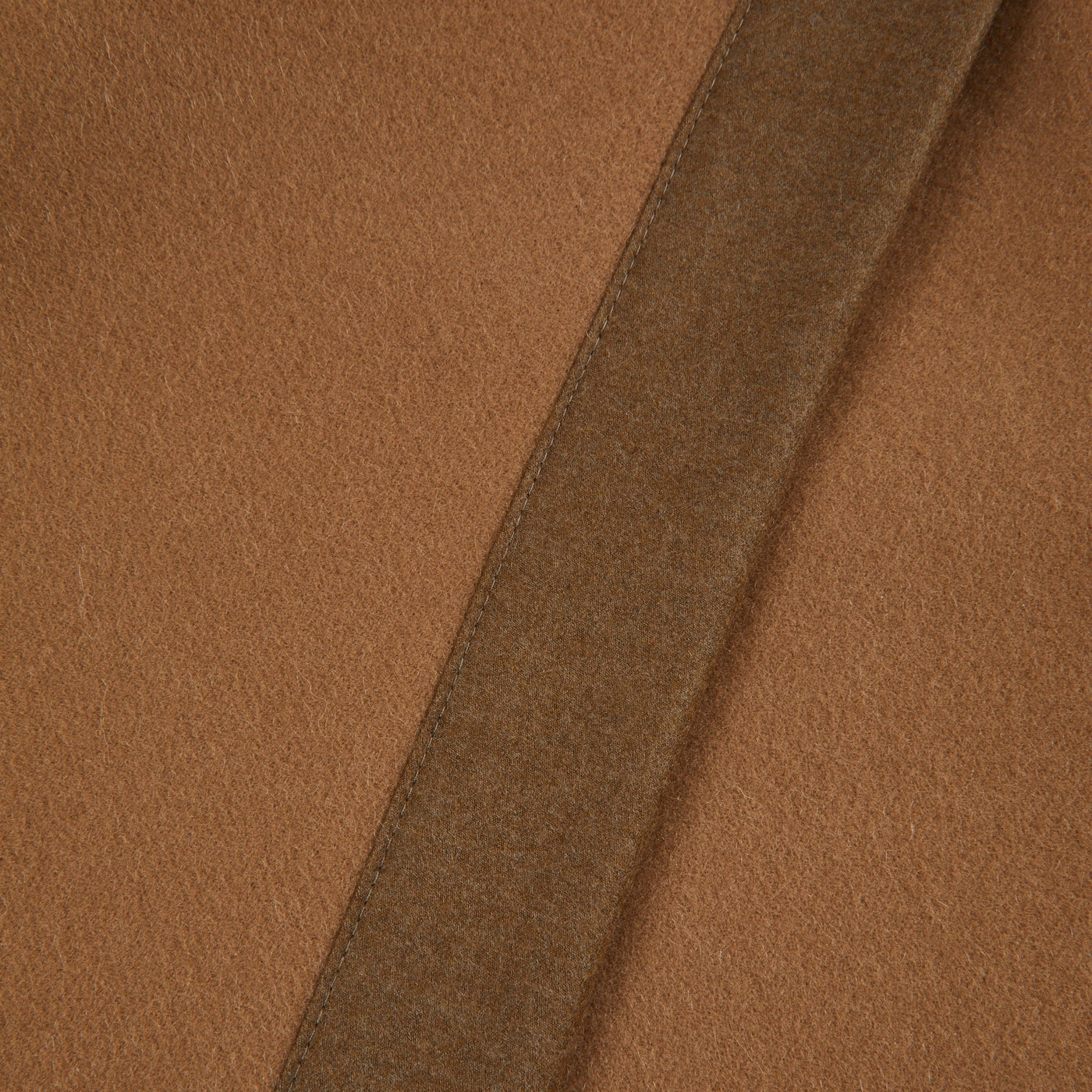 Close-up of camel wool blanket hem detail showing tonal border trim.