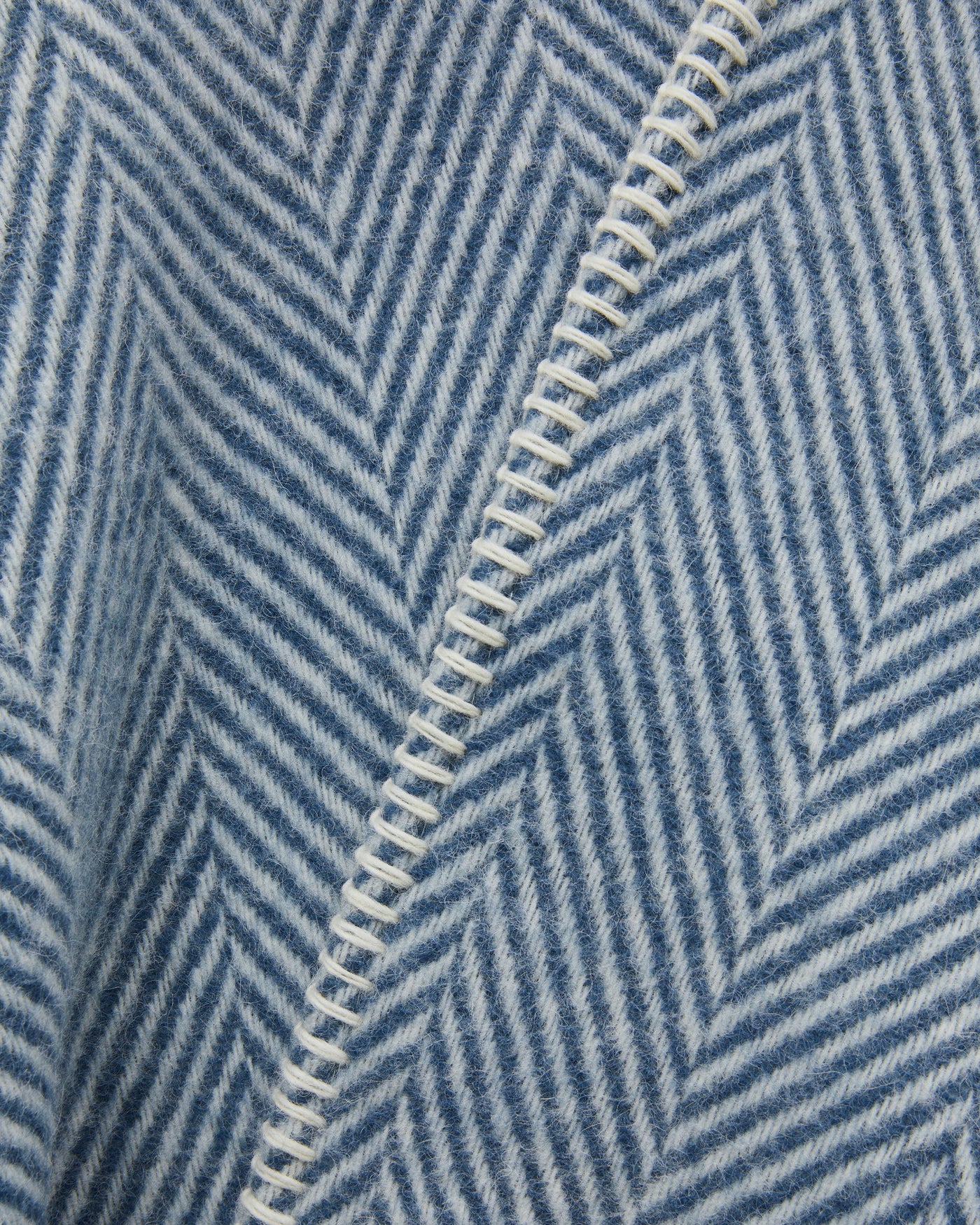 Close-up of slate blue herringbone wool with ivory whipstitch edge detail.