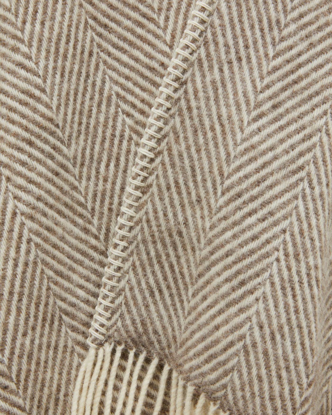 Close-up of oatmeal herringbone weave with blanket-stitch edge trim and fringe detail.