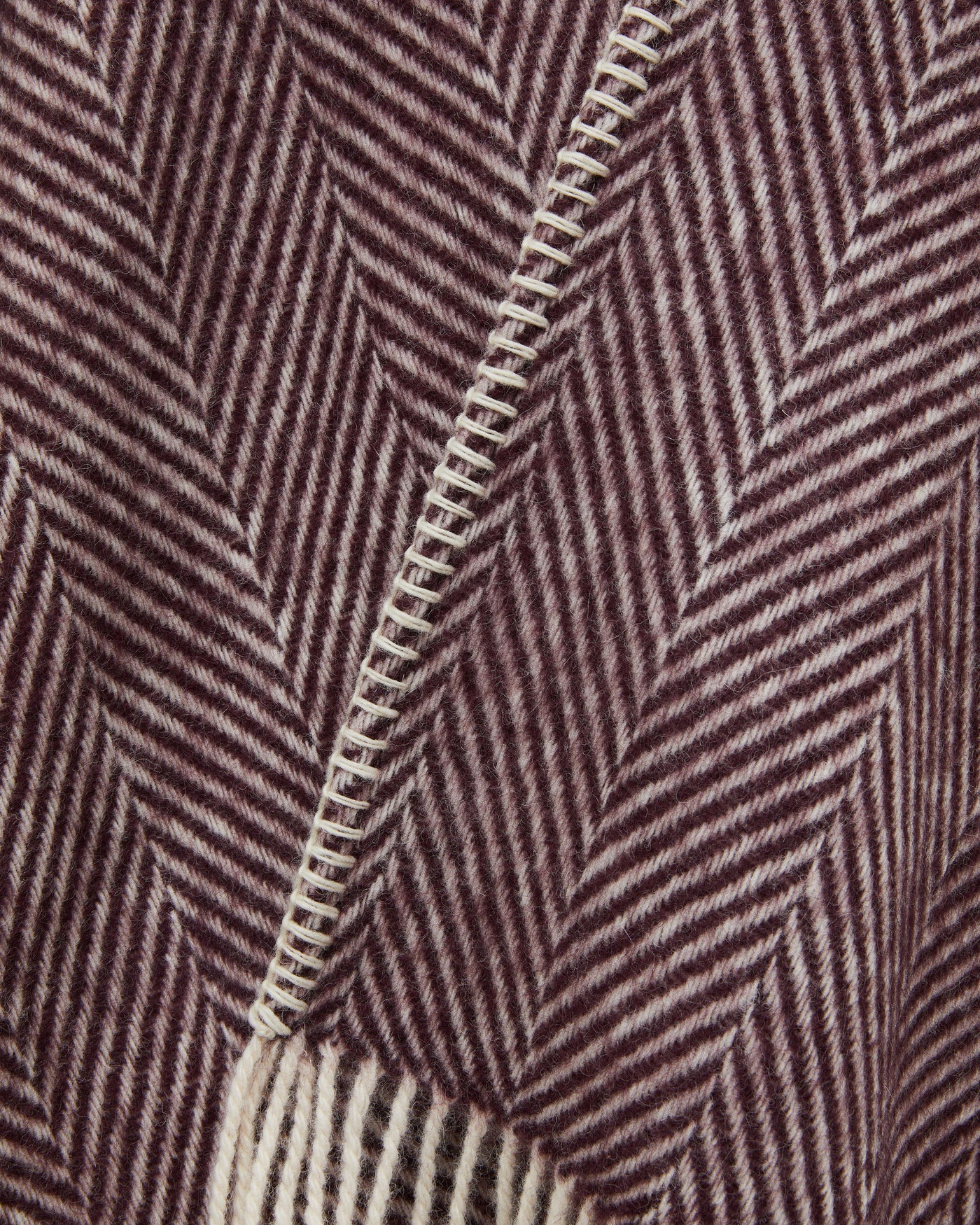 Close-up of burgundy and ivory herringbone wool weave with blanket-stitch edge detail.