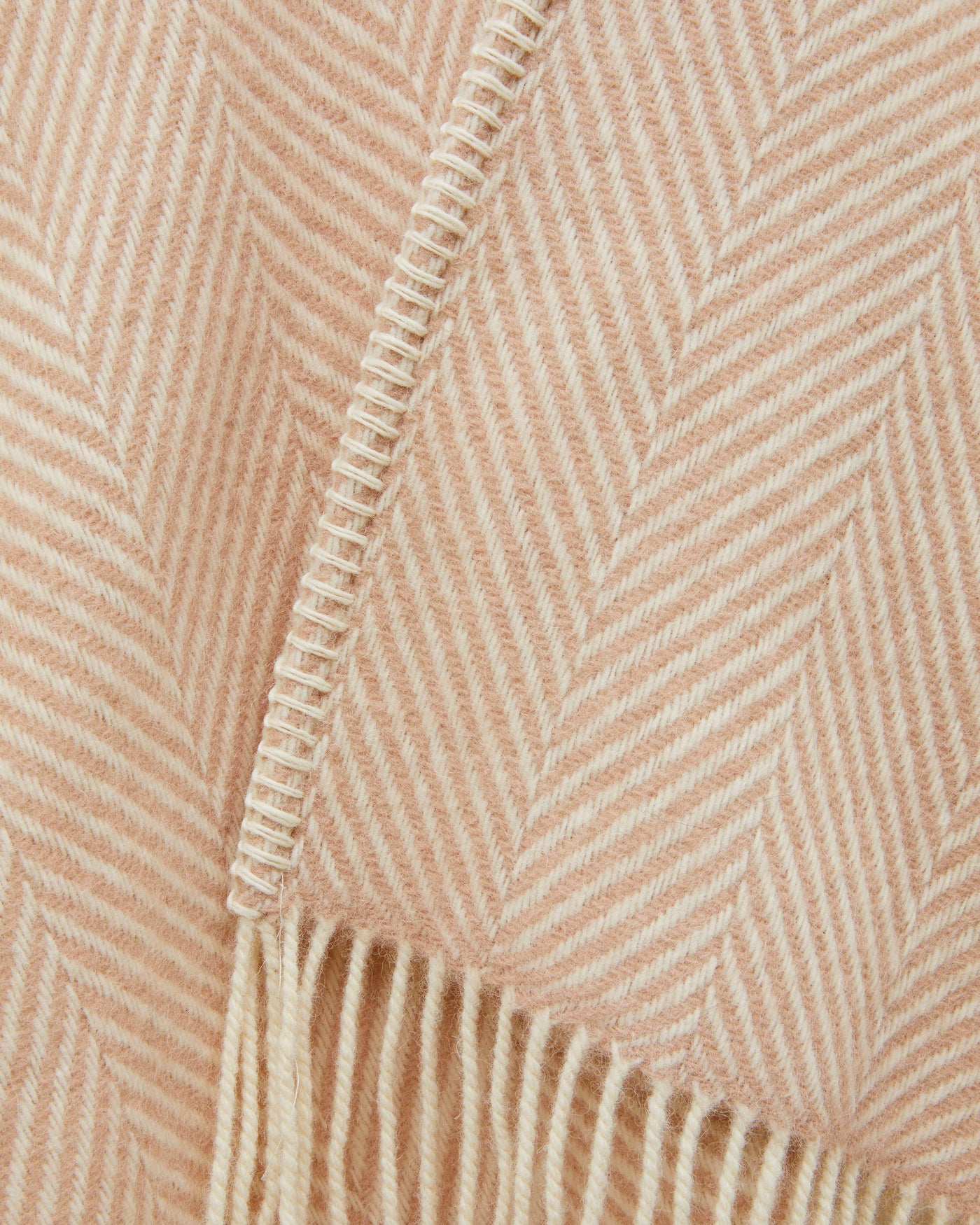 Close-up of blush herringbone weave with ivory blanket-stitch edge and fringe trim.