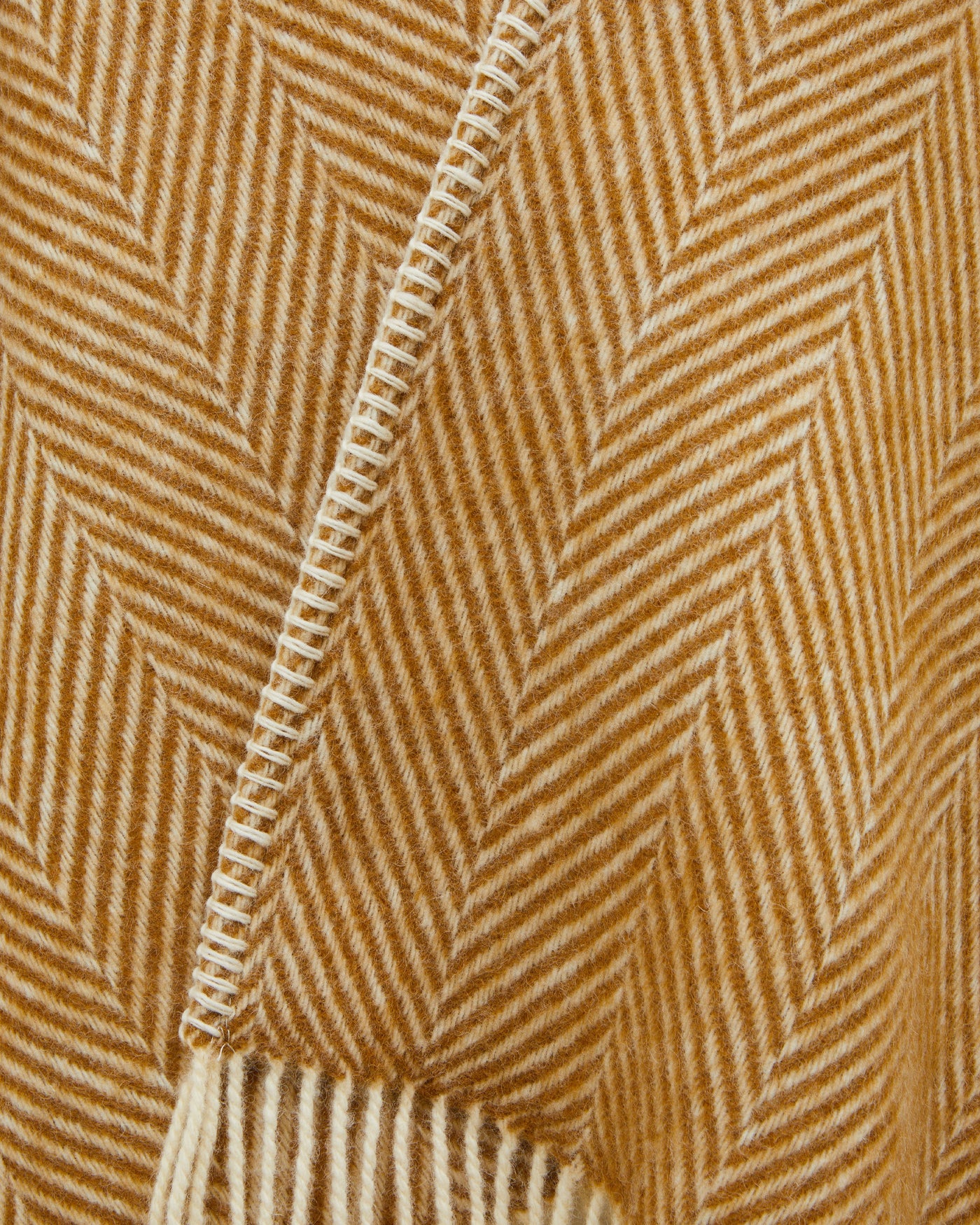 Close-up of amber herringbone weave with ivory blanket-stitch edge and fringe detail.