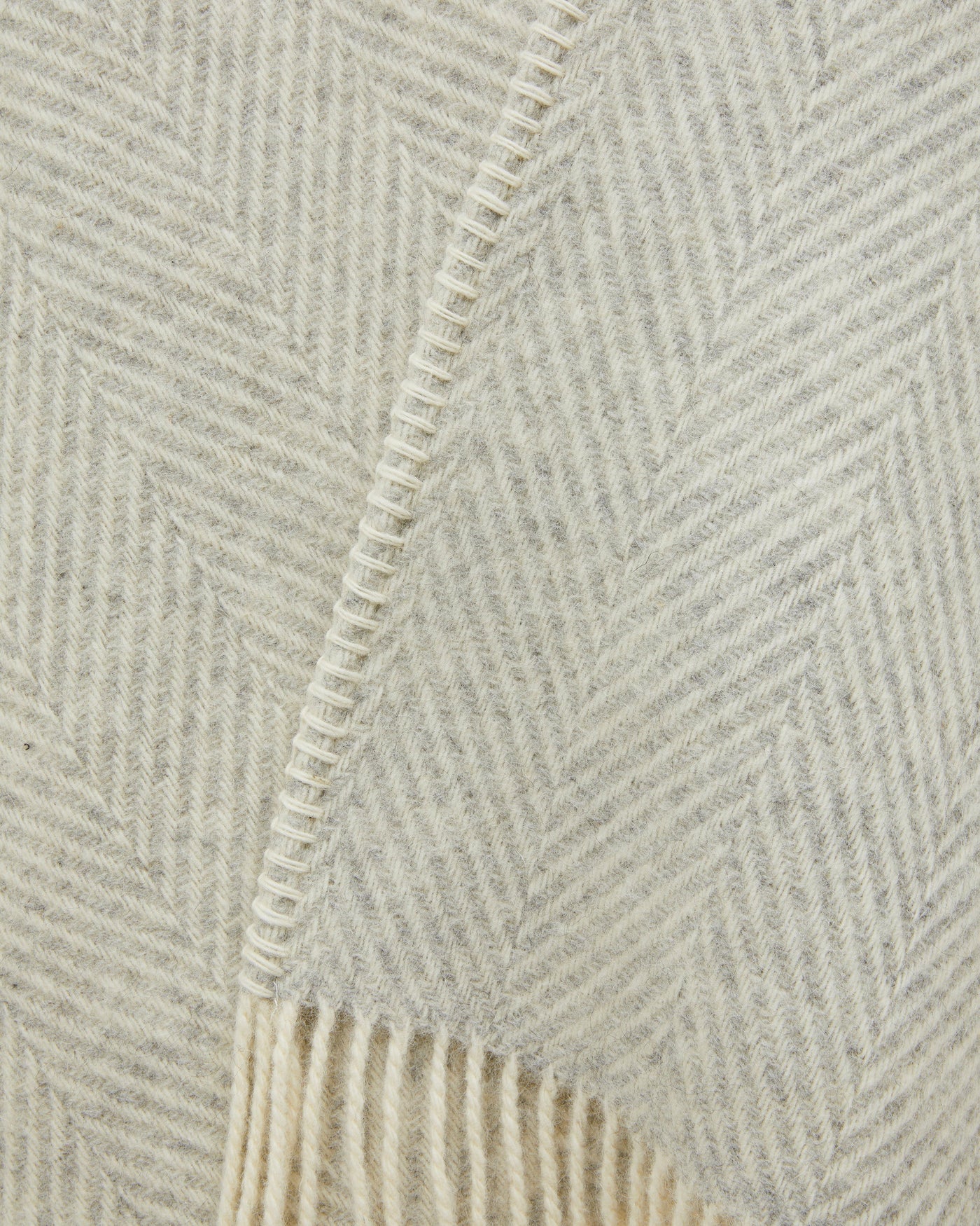 Close-up of ivory herringbone weave with blanket-stitched edge seam and fringe detail.