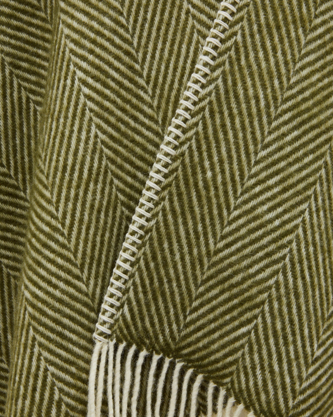 Close-up of olive herringbone weave with cream blanket-stitch edge and fringe detail.
