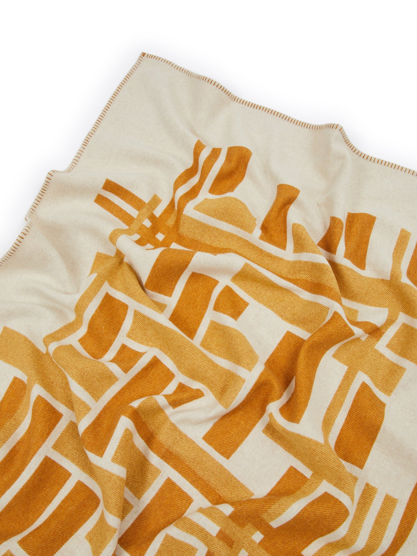 Close-up of Lanerossi Metropolis throw, amber geometric pattern on ivory with blanket-stitched edge.