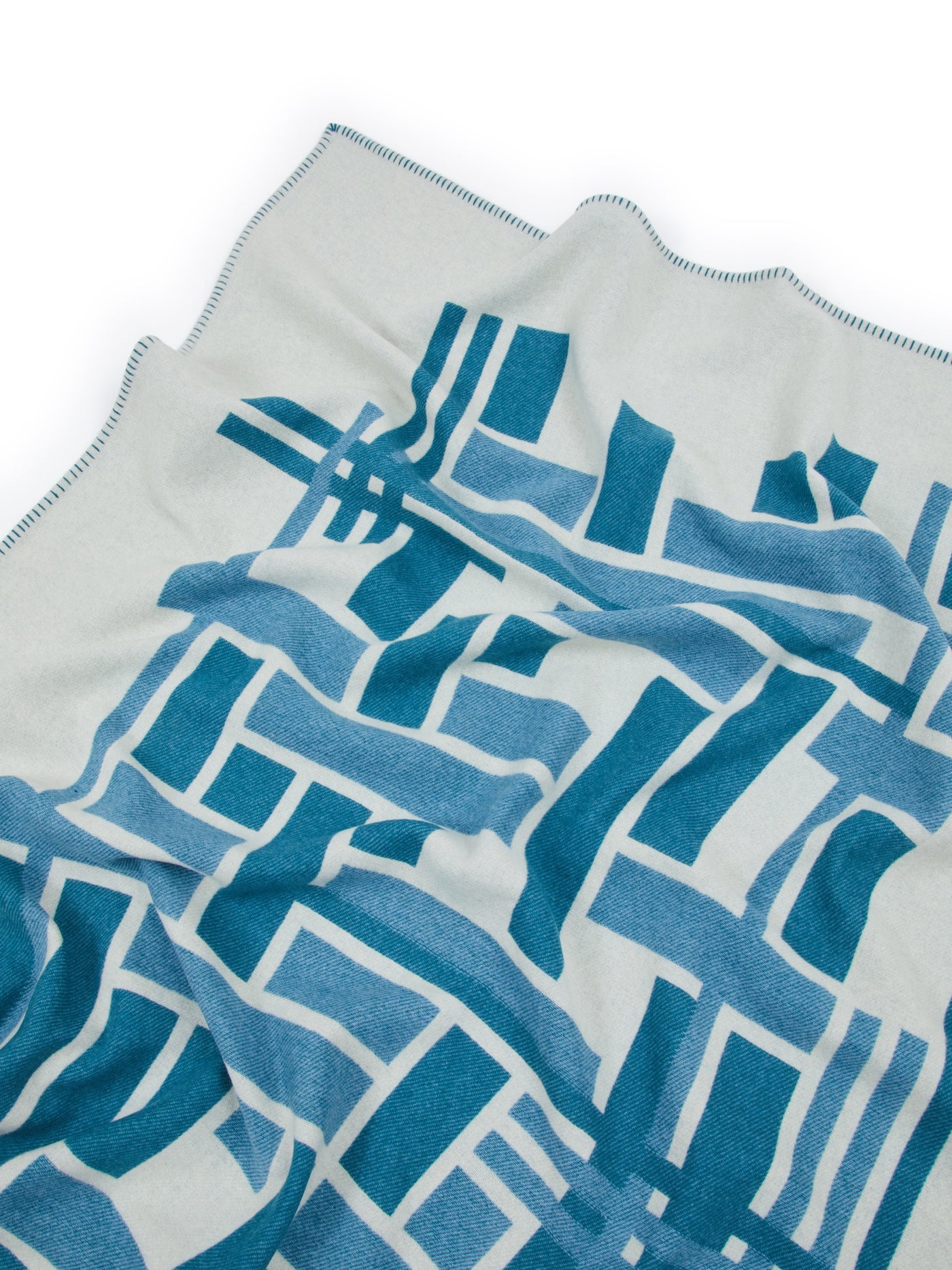 Close-up of Metropolis throw in teal geometric pattern with contrast blanket-stitch edge.