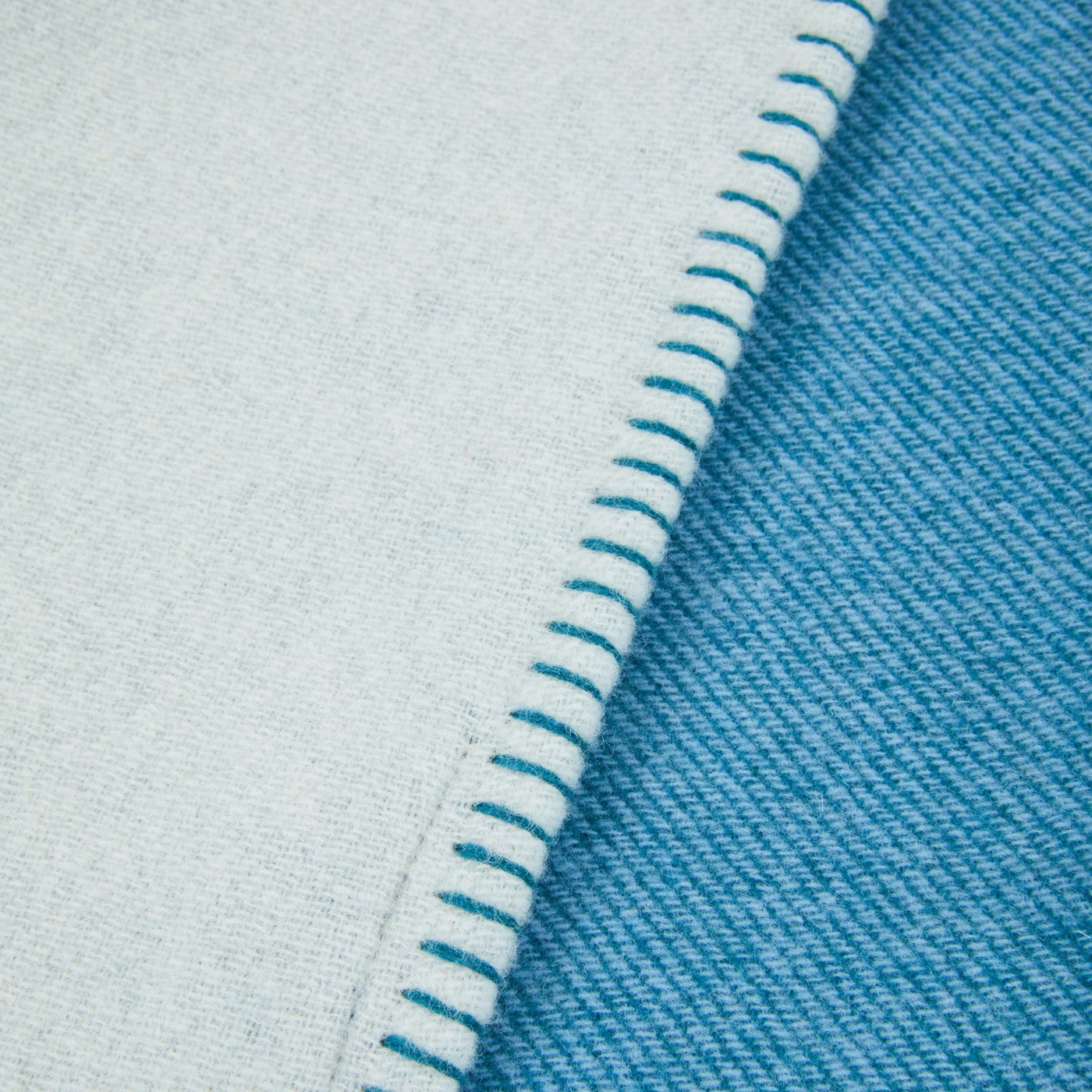 Close-up of Lanerossi Metropolis throw showing teal blanket stitch edge and reversible pale blue weave.