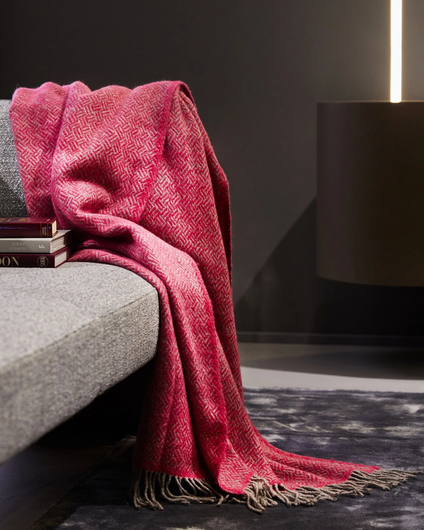 Lanerossi Mata Mata throw in raspberry, woven geometric pattern draped over grey sofa with fringe detail.