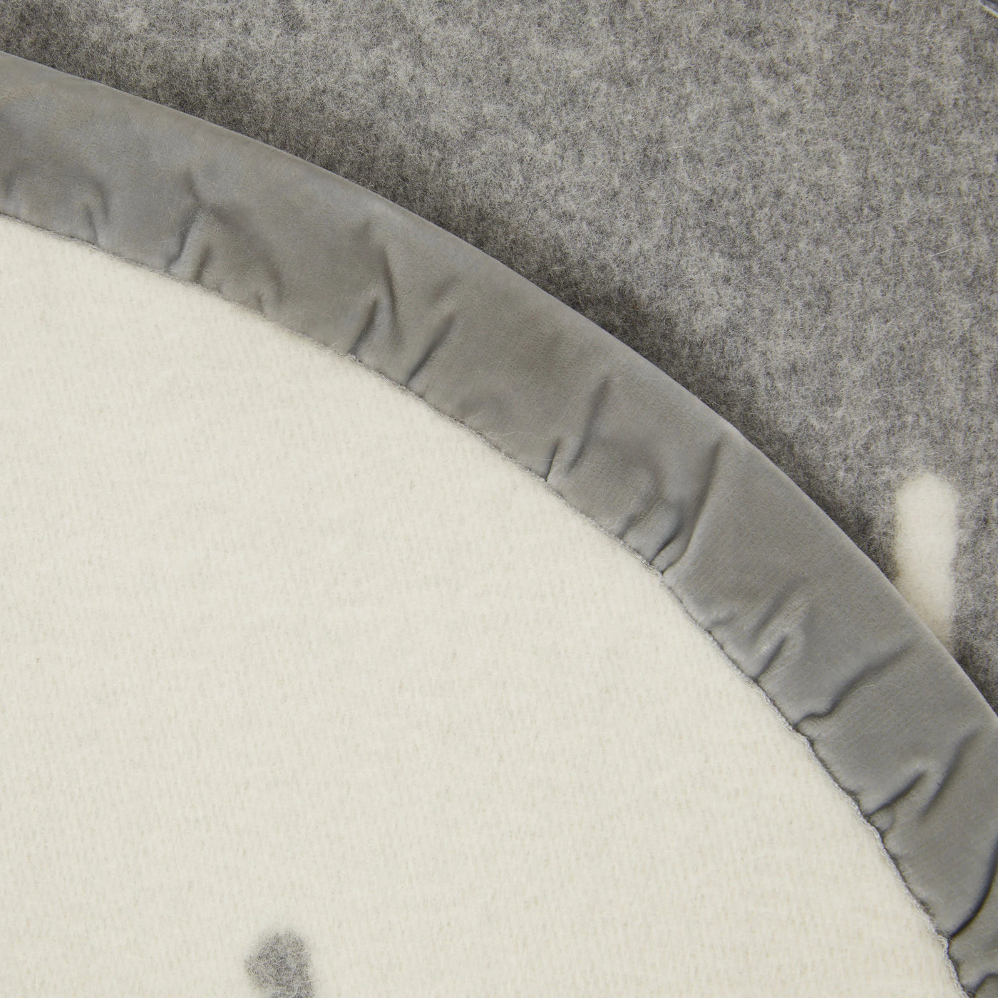 Close-up of ivory blanket edge with grey satin binding against grey felt backing.