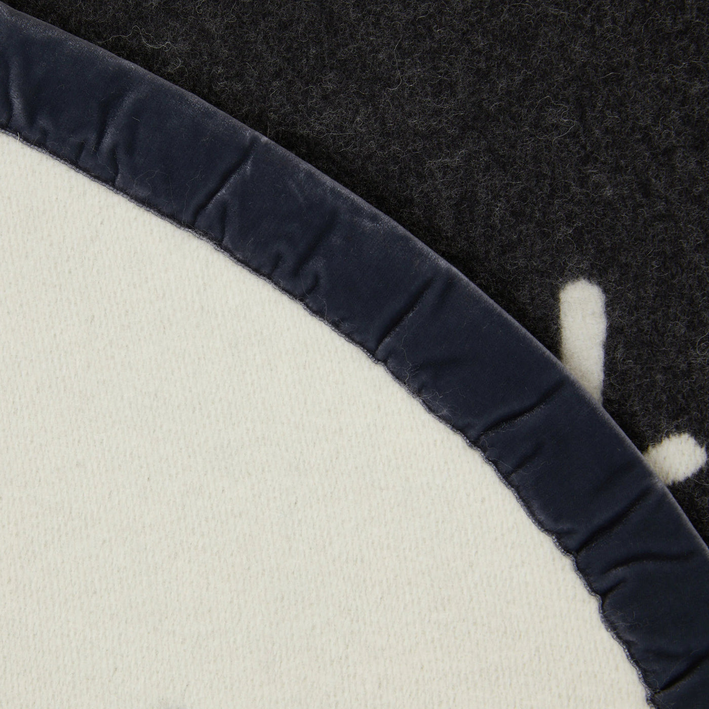 Close-up of ivory wool blanket edge with navy velvet binding detail.
