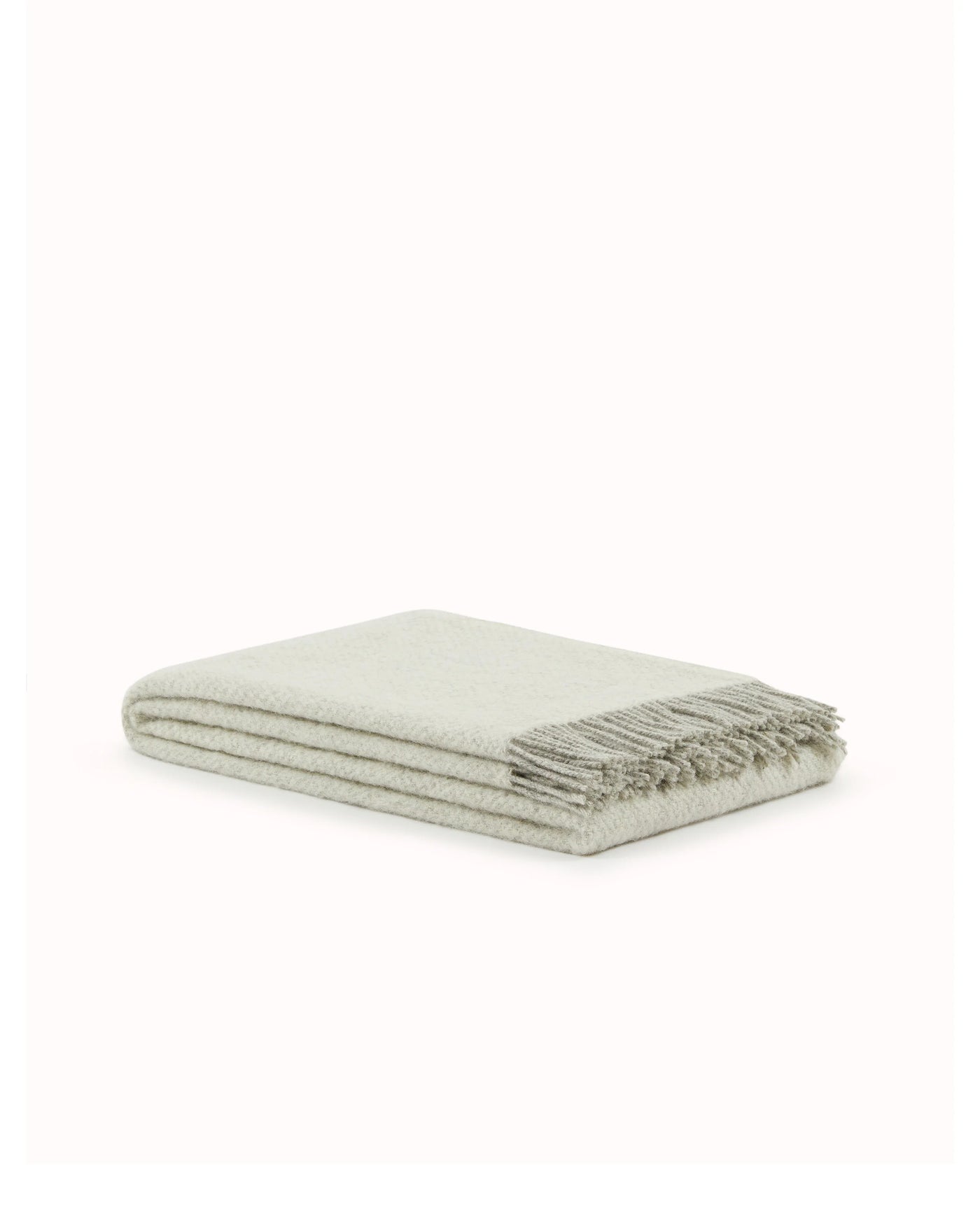 Folded sage herringbone throw with fringe trim, angled product view.