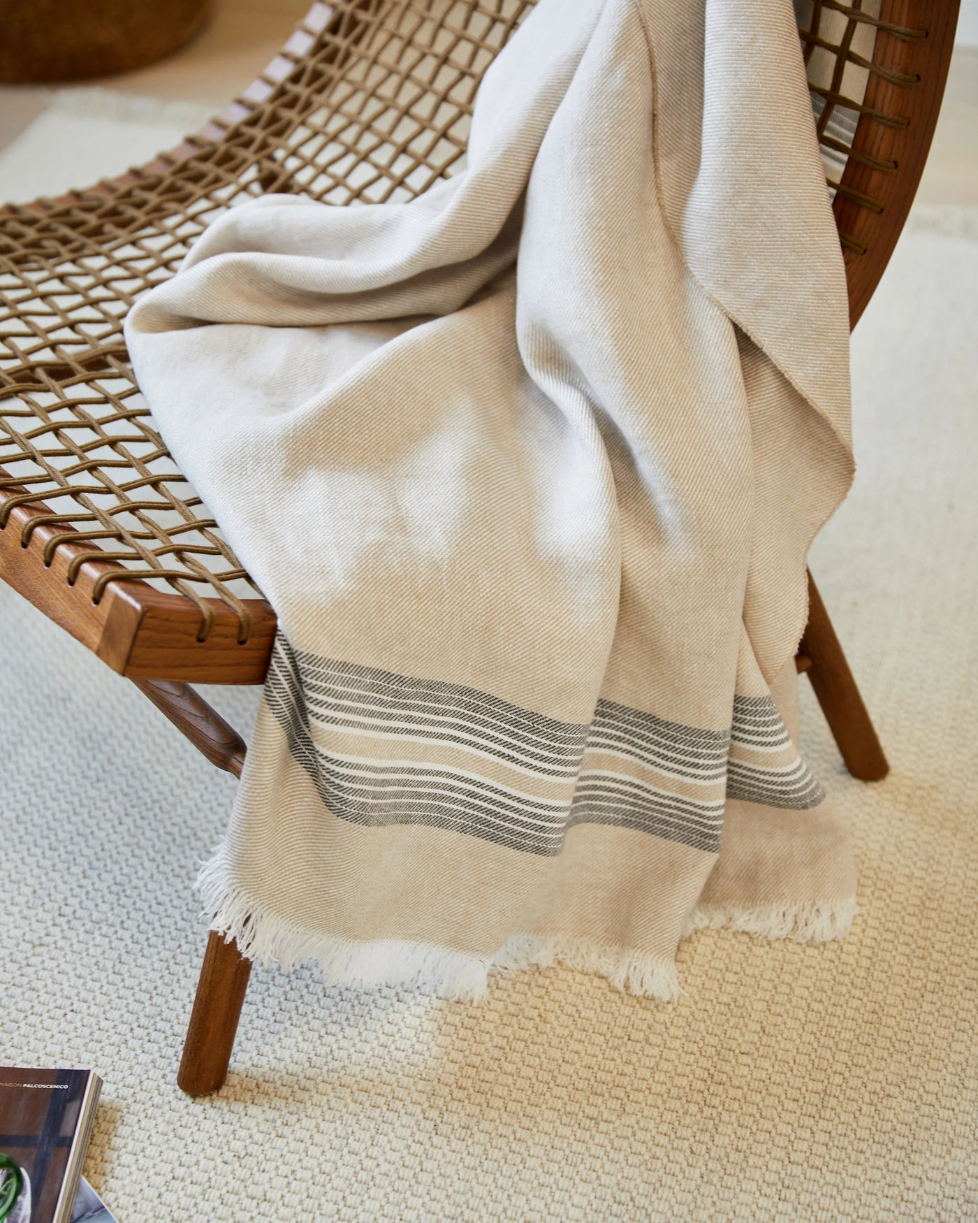 Lanerossi Palau throw in sand with grey stripes and fringe trim, draped over a woven bench.
