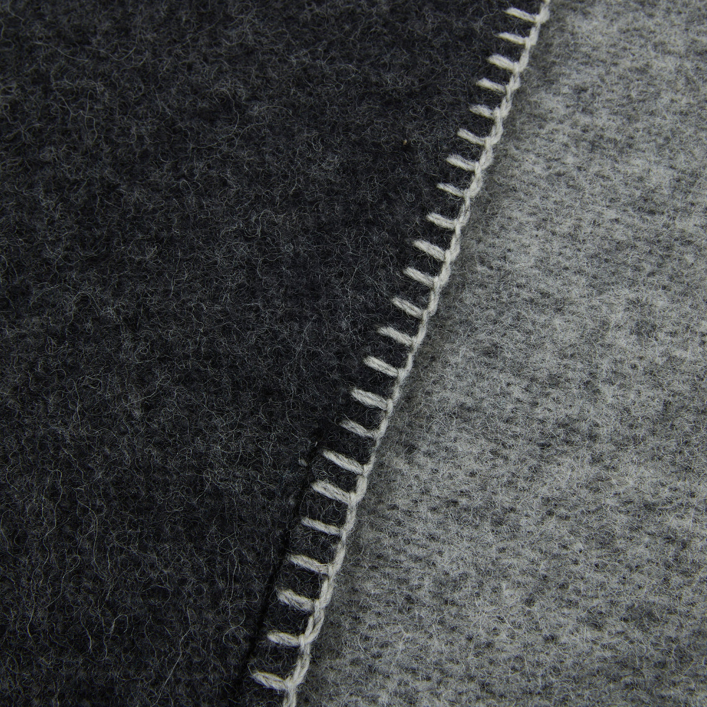 Close-up of ivory blanket stitch edge joining charcoal and grey wool sides.
