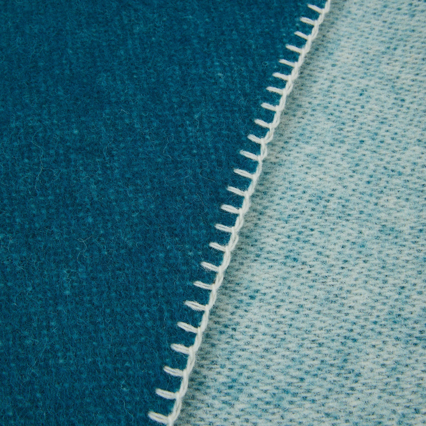 Close-up of teal and pale blue reversible wool throw with white blanket-stitch edge detail.