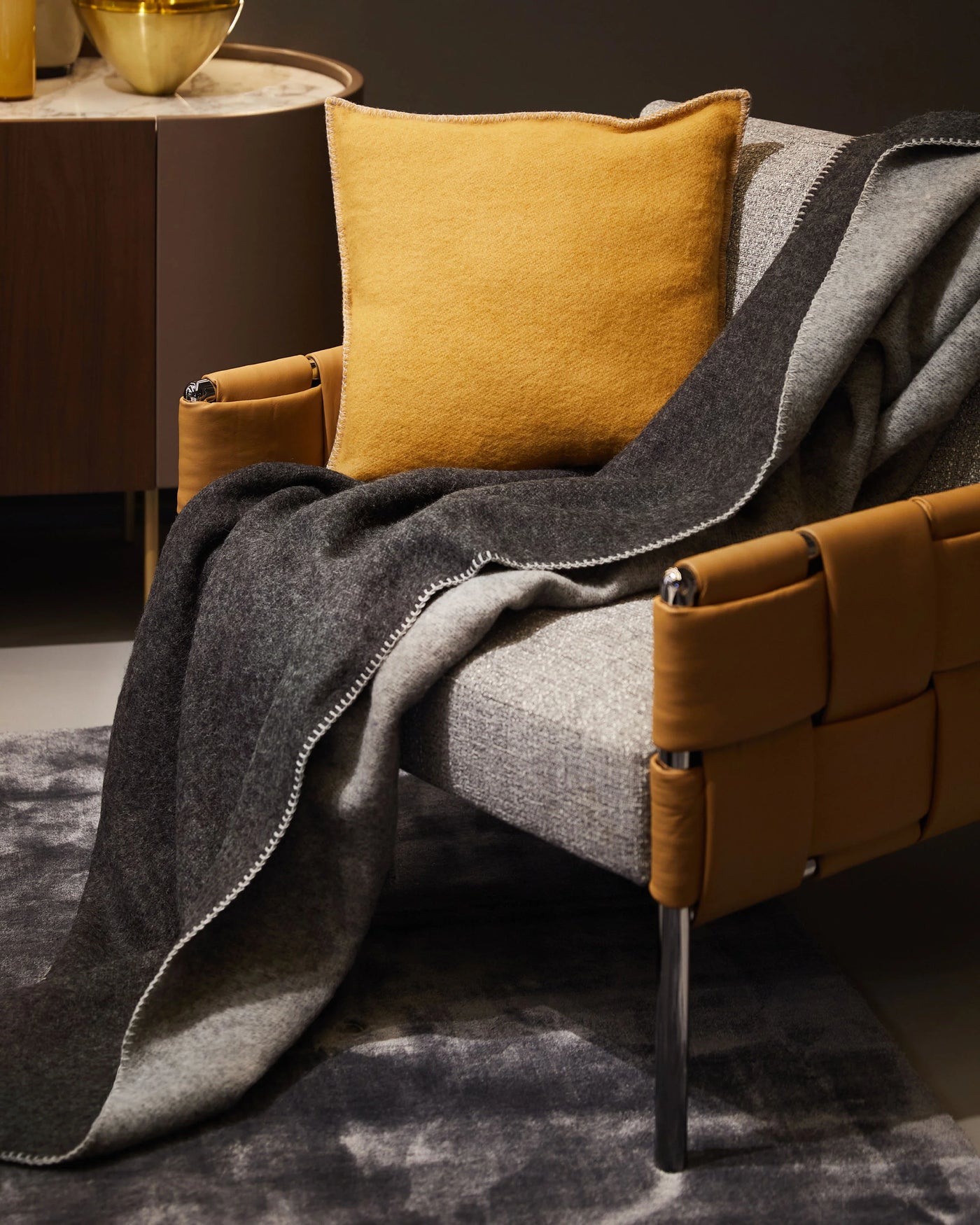 Charcoal and grey Lanerossi Southland throw draped over a tan leather chair with a mustard cushion.