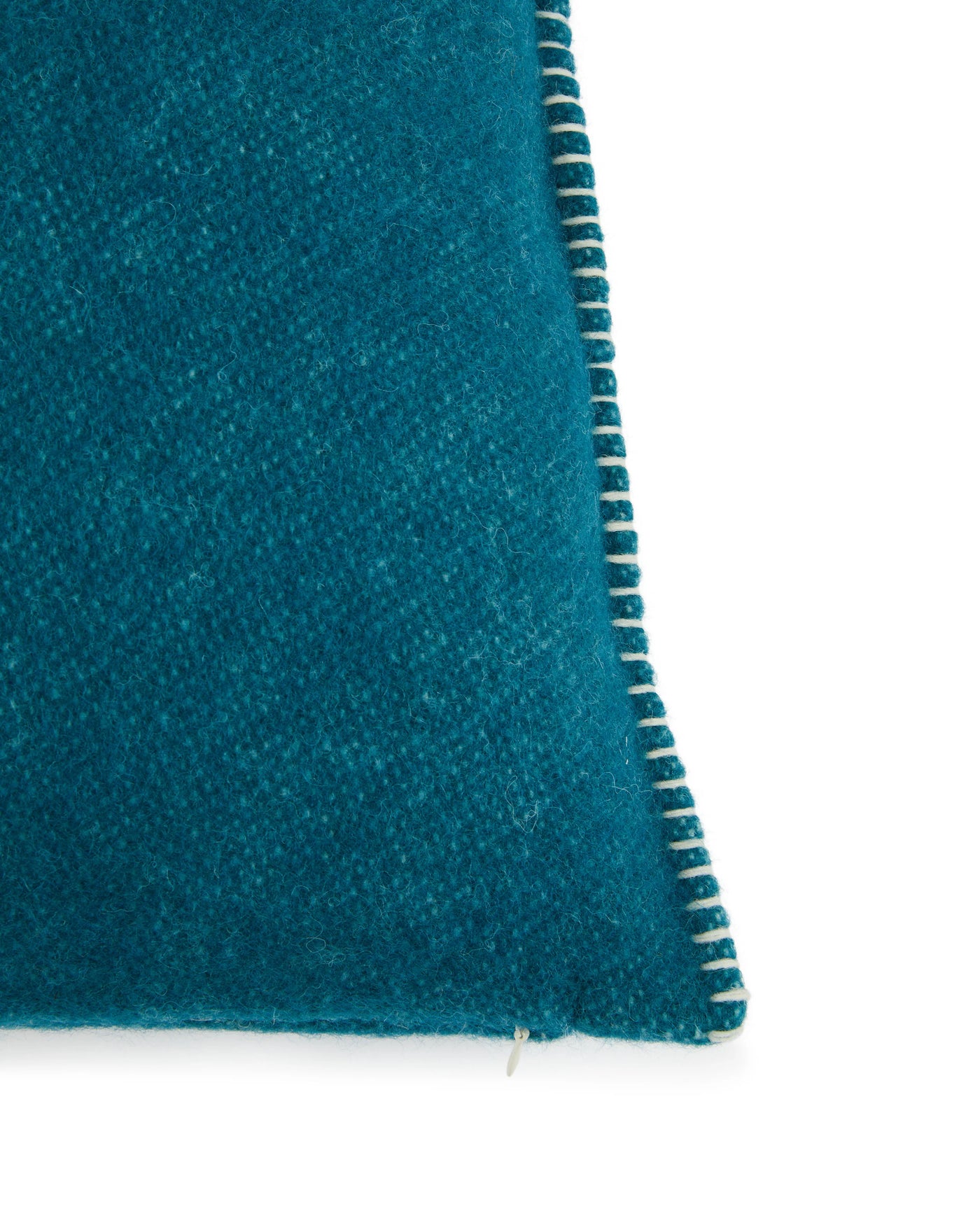 Close-up of teal wool cushion corner with ivory blanket-stitch trim detail.