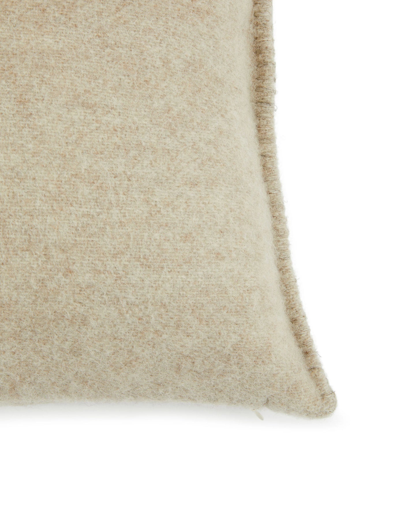 Corner detail of a sand-toned wool cushion showing whipstitch edge trim and brushed texture.