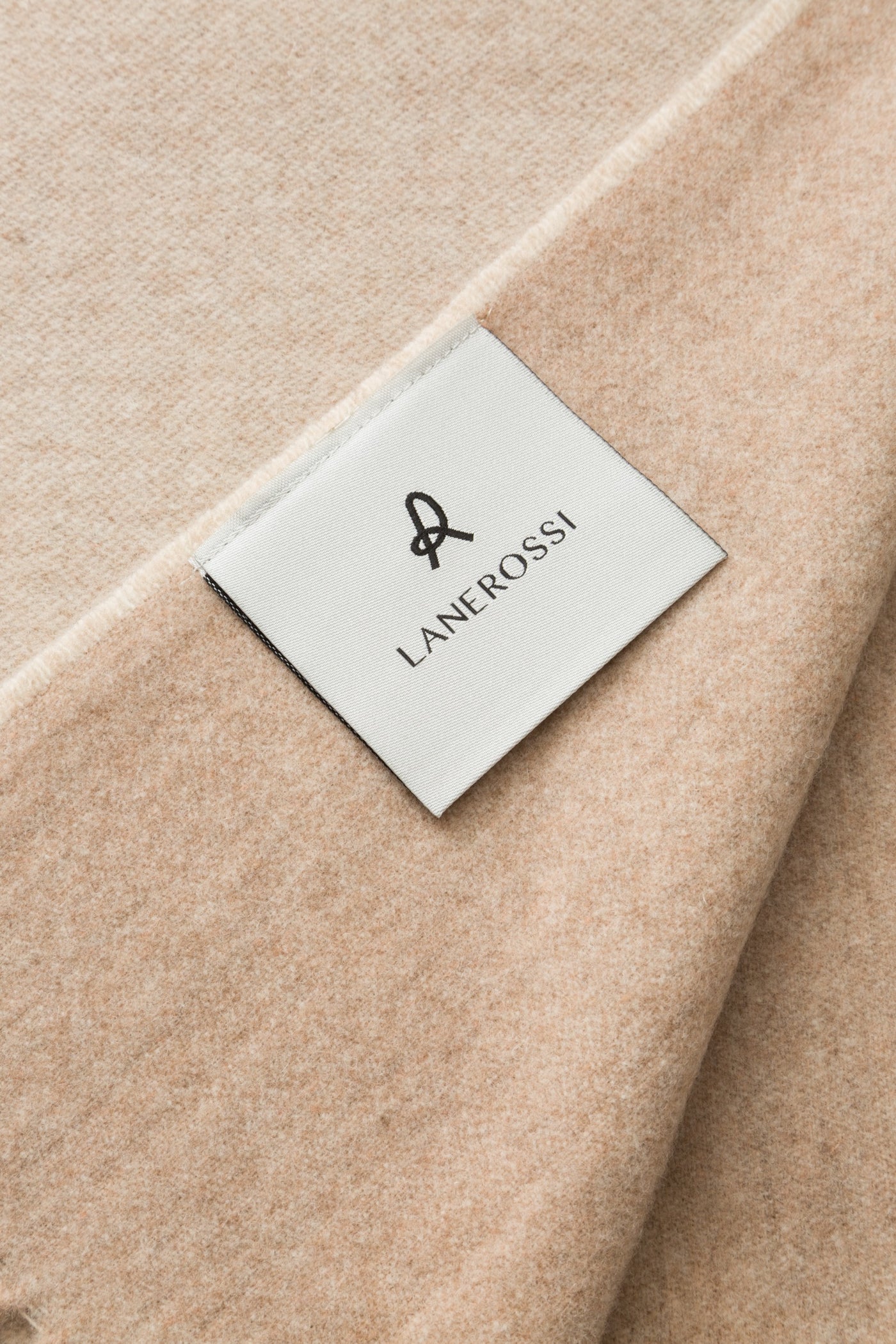 Close-up of Lanerossi Ulisse throw in sand, showing woven label on folded wool fabric.