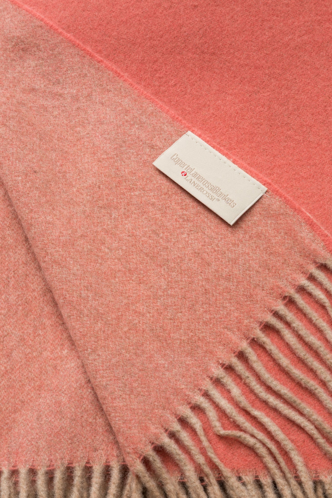 Close-up of coral and blush ombre wool throw with fringe edge and woven brand label.