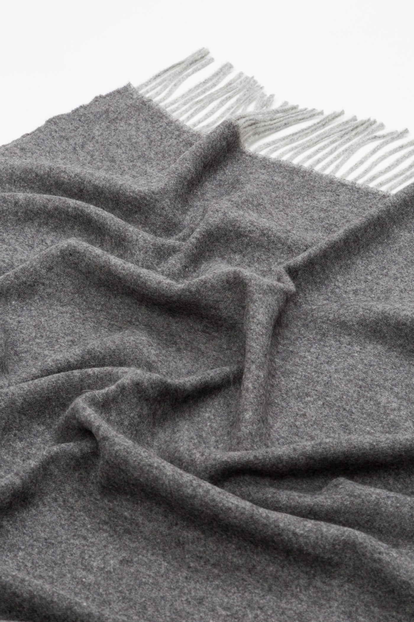 Close-up of draped charcoal wool throw with ivory fringe trim detail.